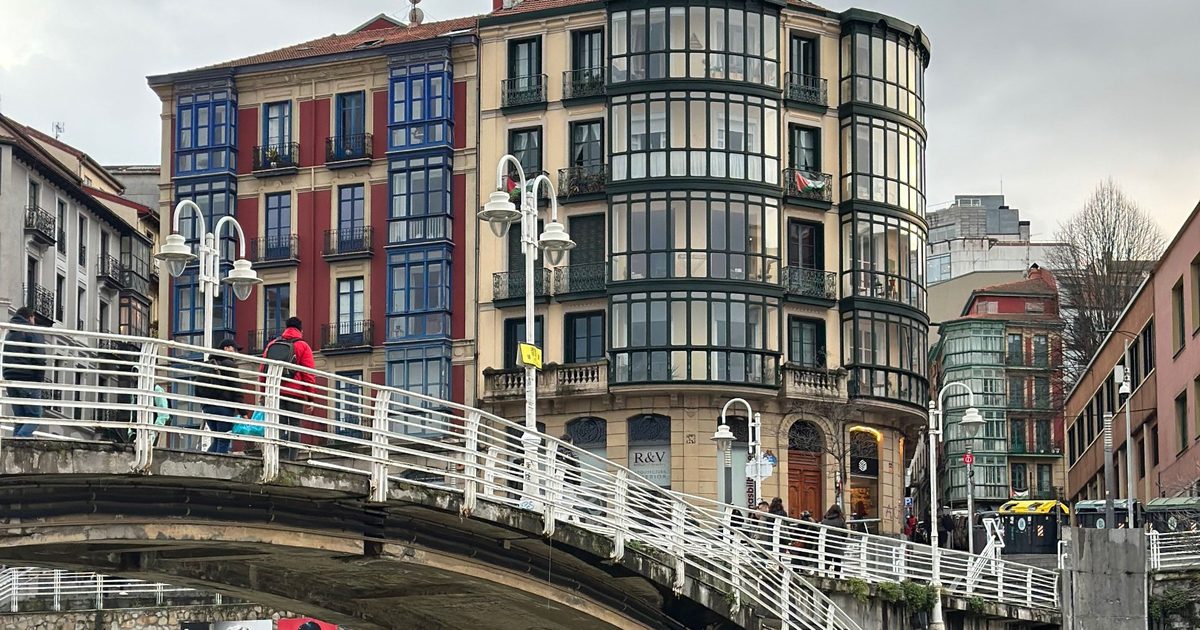 Pasarela blanca sobre la ría de Bilbao con edificios con miradores de cristal al fondo
